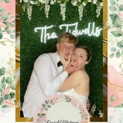 Bride and groom posing together at their wedding photo booth with a neon name sign