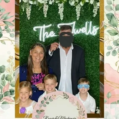 Family with kids smiling at a wedding photo booth with a greenery backdrop
